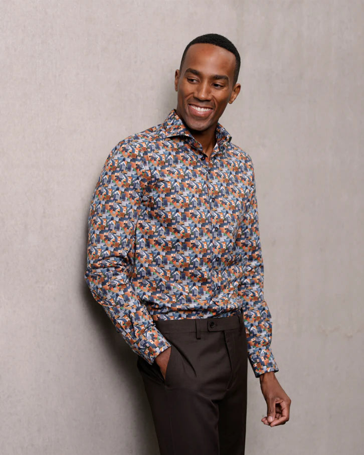 Man wearing a patterned shirt and dark pants against a plain background
