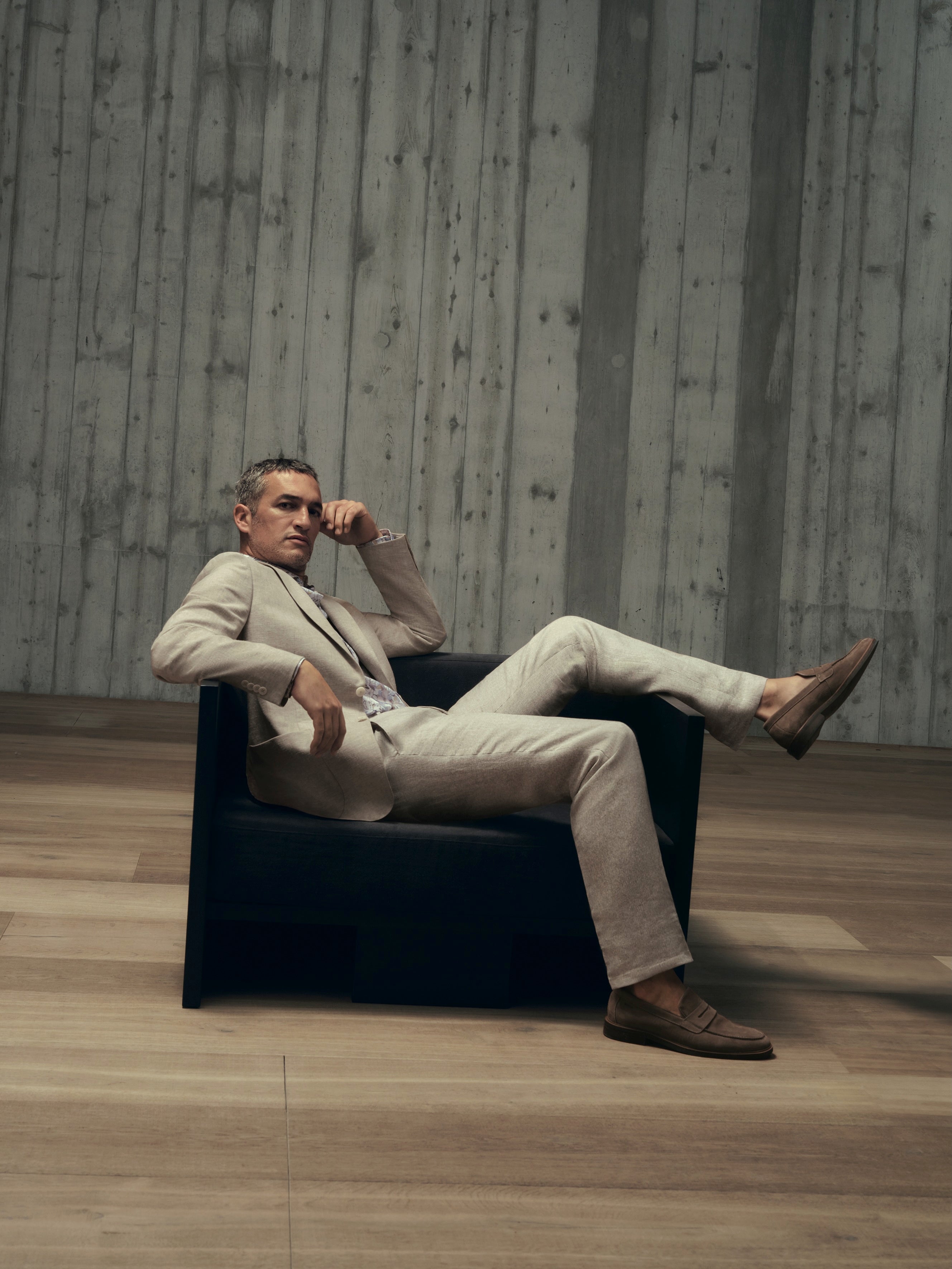 Man sitting on a black chair in a minimalistic room with concrete walls.