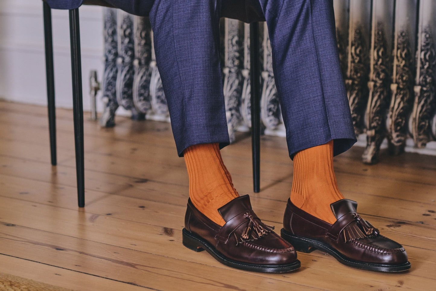 Person wearing brown loafers and orange socks on a wooden floor.