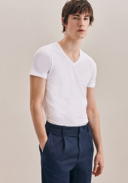 Man wearing a white V-neck shirt and navy pants against a plain background