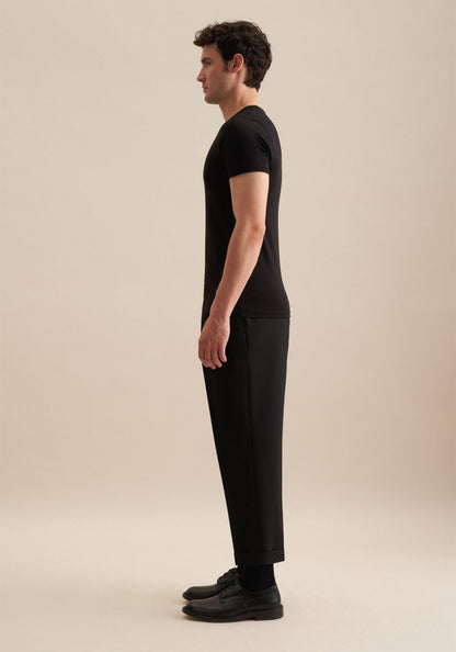 Man wearing a black t-shirt and pants standing against a beige background