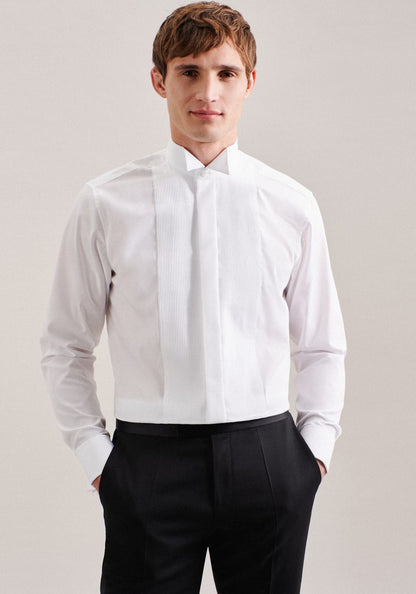 Man wearing a white dress shirt with a bow tie and black pants against a plain background