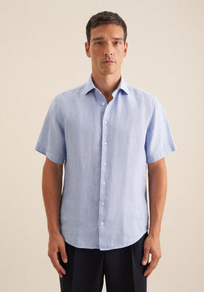 Man wearing a light blue short-sleeve shirt against a beige background