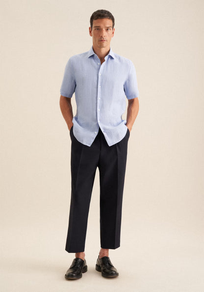 Man wearing a light blue checkered shirt and black pants on a beige background