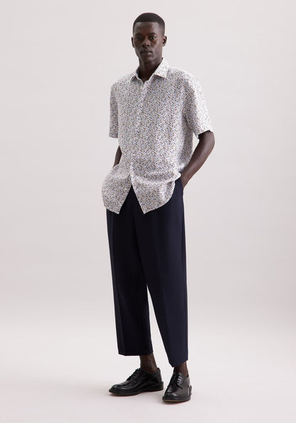Man wearing a patterned shirt and black pants on a white background