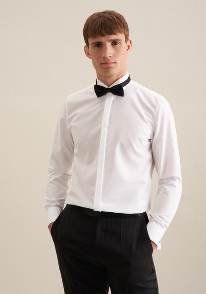 Man wearing a white dress shirt with a black bow tie and black pants on a beige background