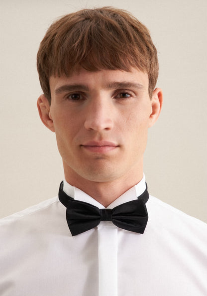 Man wearing a black bow tie and white shirt against a plain background