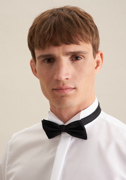 Man wearing a white dress shirt and black bow tie against a beige background