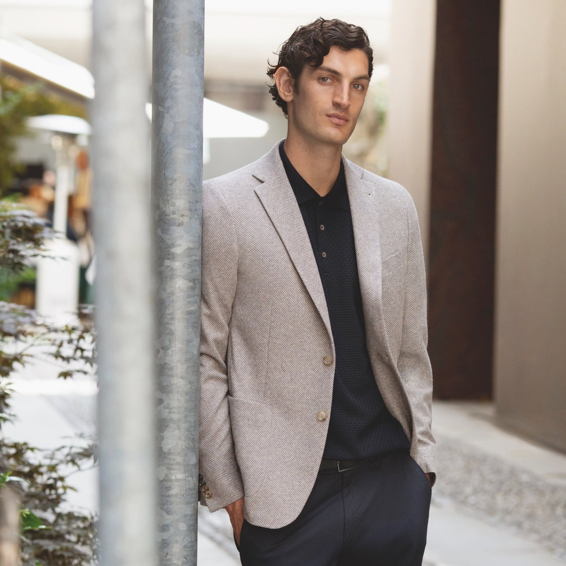 Man in a light gray blazer and black pants standing outdoors.