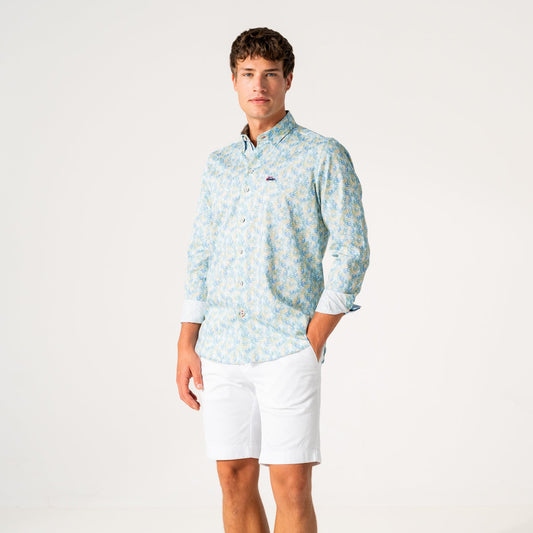 A man modeling a light blue and white patterned long-sleeve button-down shirt with white shorts, standing against a plain white studio background.