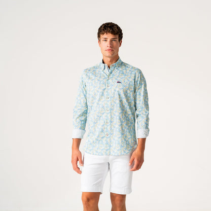 A young man modeling a light blue and white patterned long-sleeve button-down shirt with white shorts, standing against a plain white studio background.