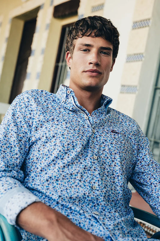 Man wearing a blue patterned shirt sitting outdoors with a building in the background
