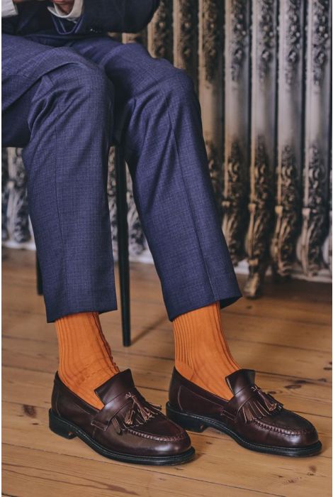 Person wearing blue pants, orange socks, and brown loafers with a decorative wall in the background.