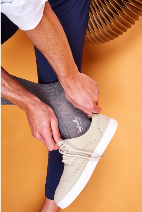 Person tying a beige sneaker on a mustard yellow background