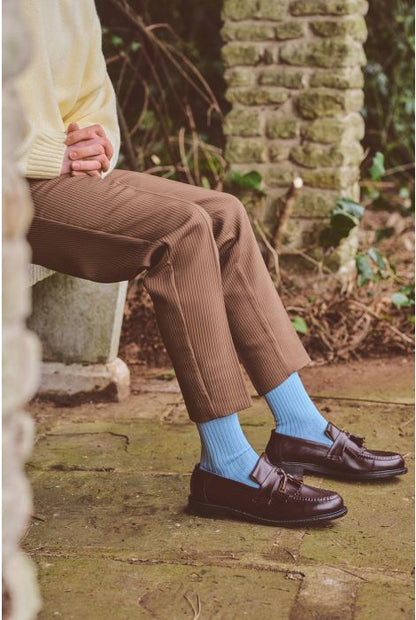 Person wearing brown corduroy pants, a yellow sweater, and blue socks sitting on a stone bench.