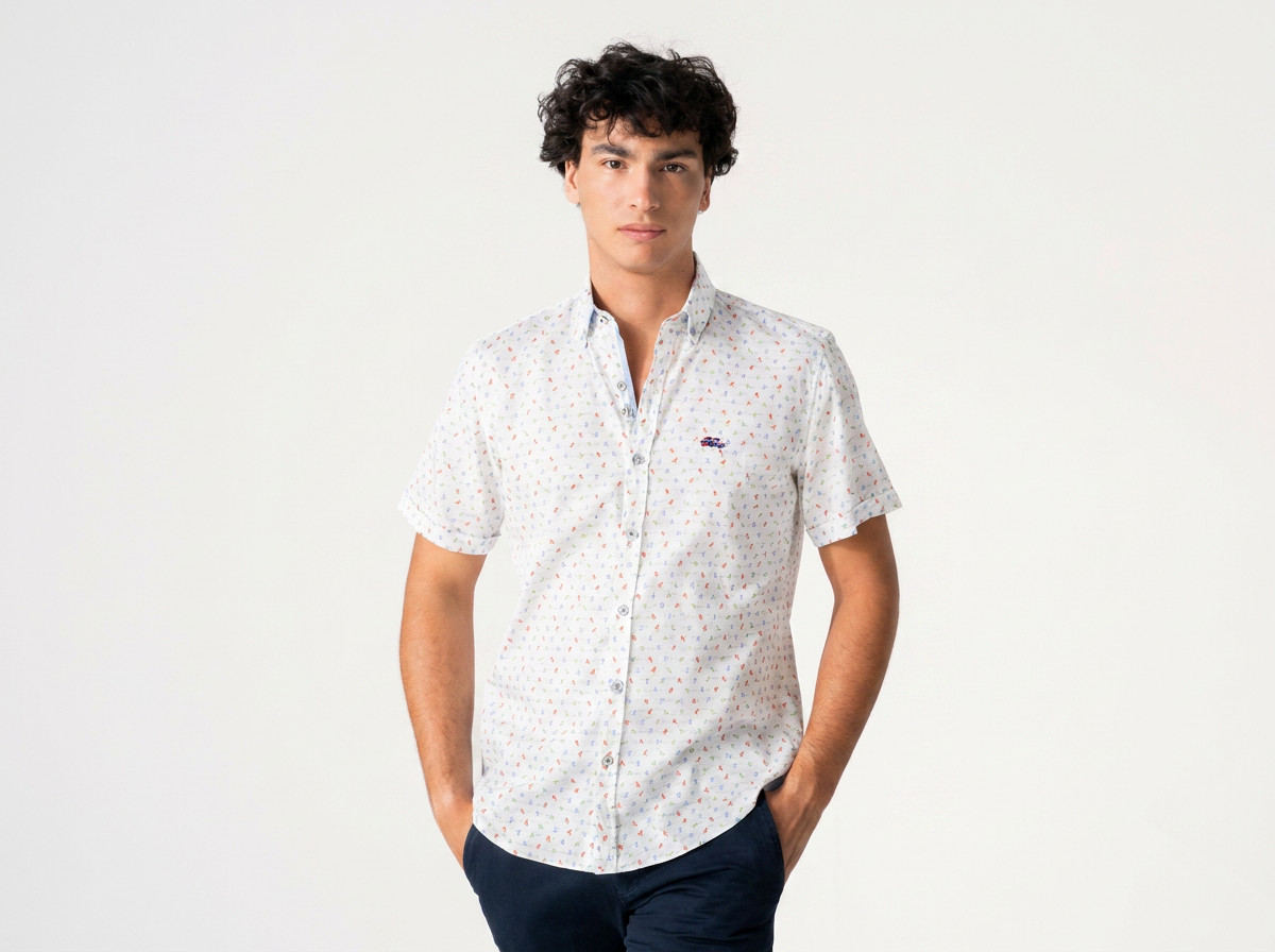 A man modeling a short-sleeve button-up shirt with a small multicolor geometric pattern on a white base, paired with dark navy pants, against a plain white studio background.