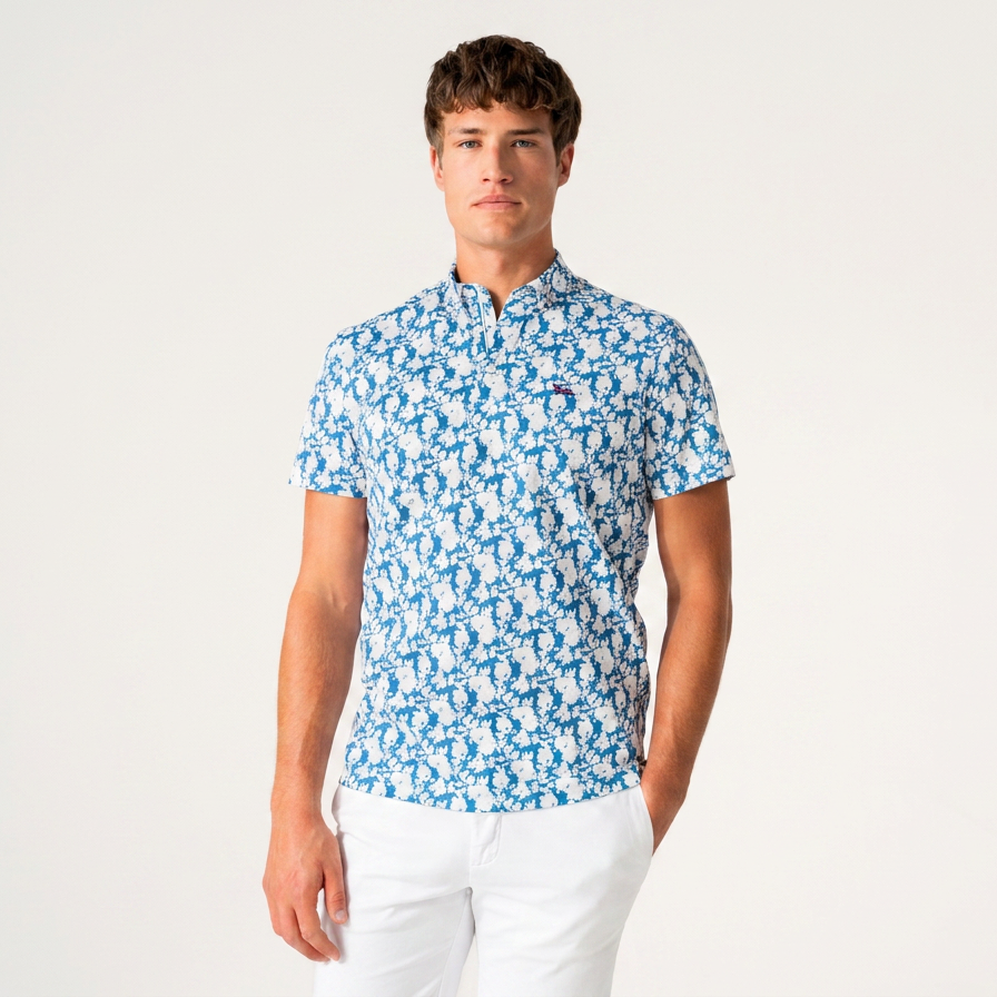 A man modeling a short-sleeve polo shirt with a blue and white repeating pattern, paired with white trousers, against a plain light gray studio background.