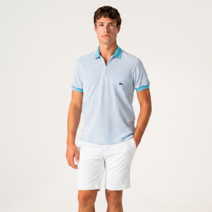 A man modeling a light blue polo shirt with contrasting turquoise blue collar and sleeve trim, paired with white shorts, against a clean white studio background.