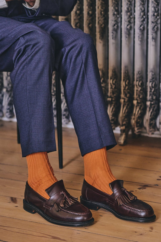 Person wearing navy suit, orange socks, and brown loafers sitting on a wooden floor.