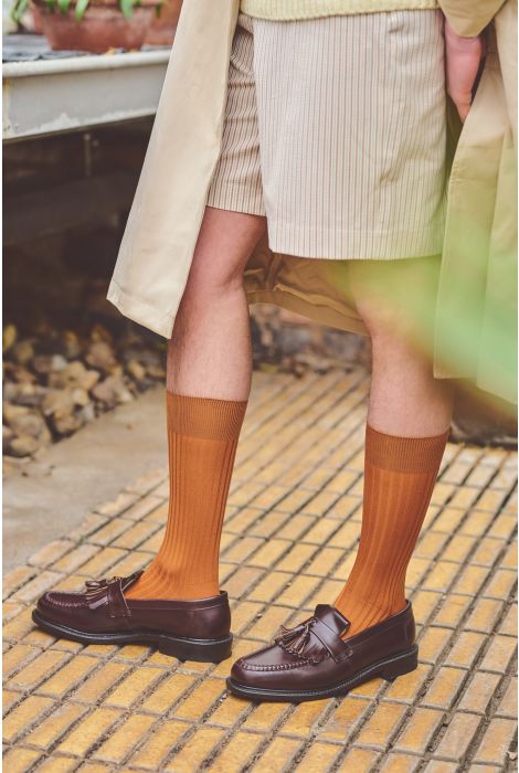 Person wearing brown socks and loafers on a tiled floor.
