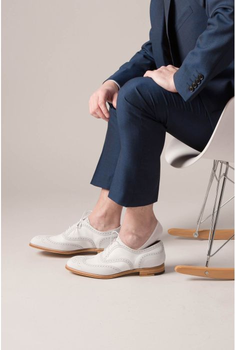 Person wearing a navy suit and white shoes sitting on a chair.