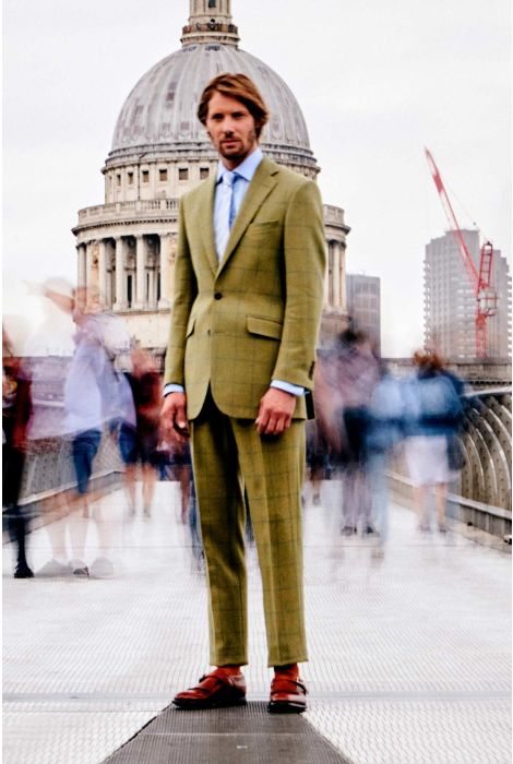 Man in a green suit standing in front of a cityscape with a blurred crowd