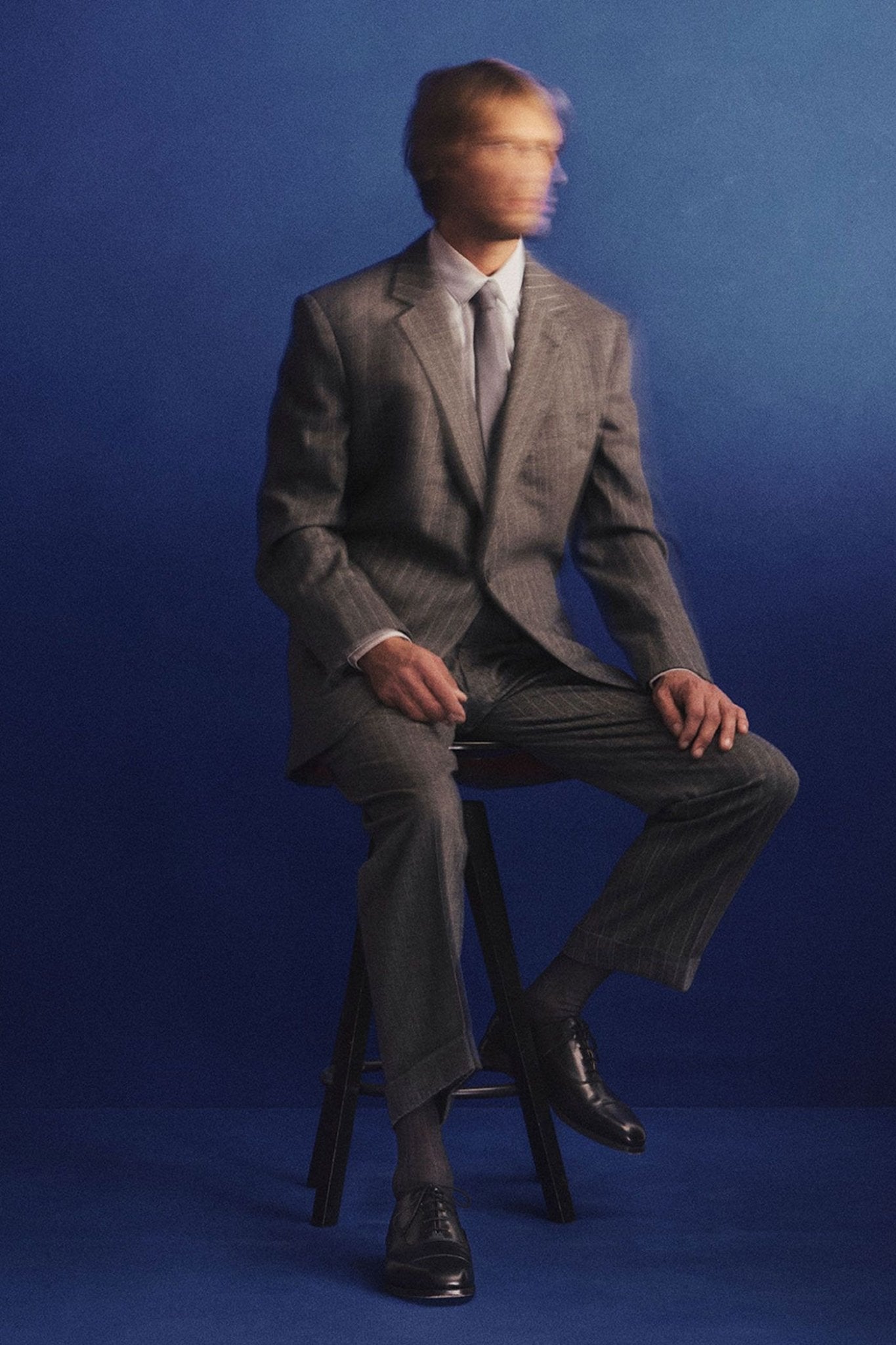 Man in a gray suit sitting on a stool against a blue background