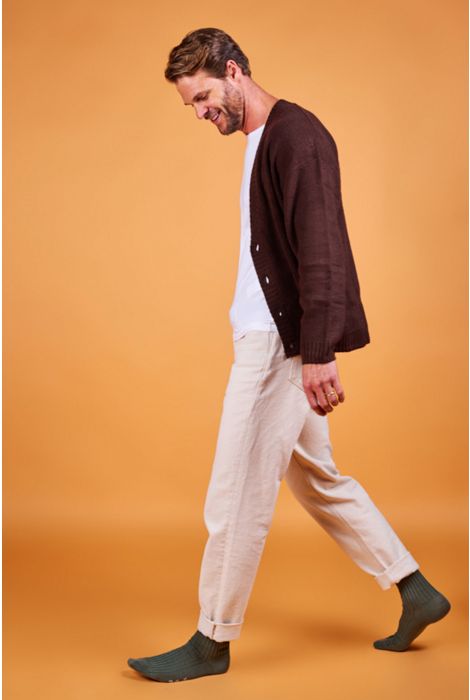 Man wearing a brown cardigan, white shirt, beige pants, and dark socks on an orange background