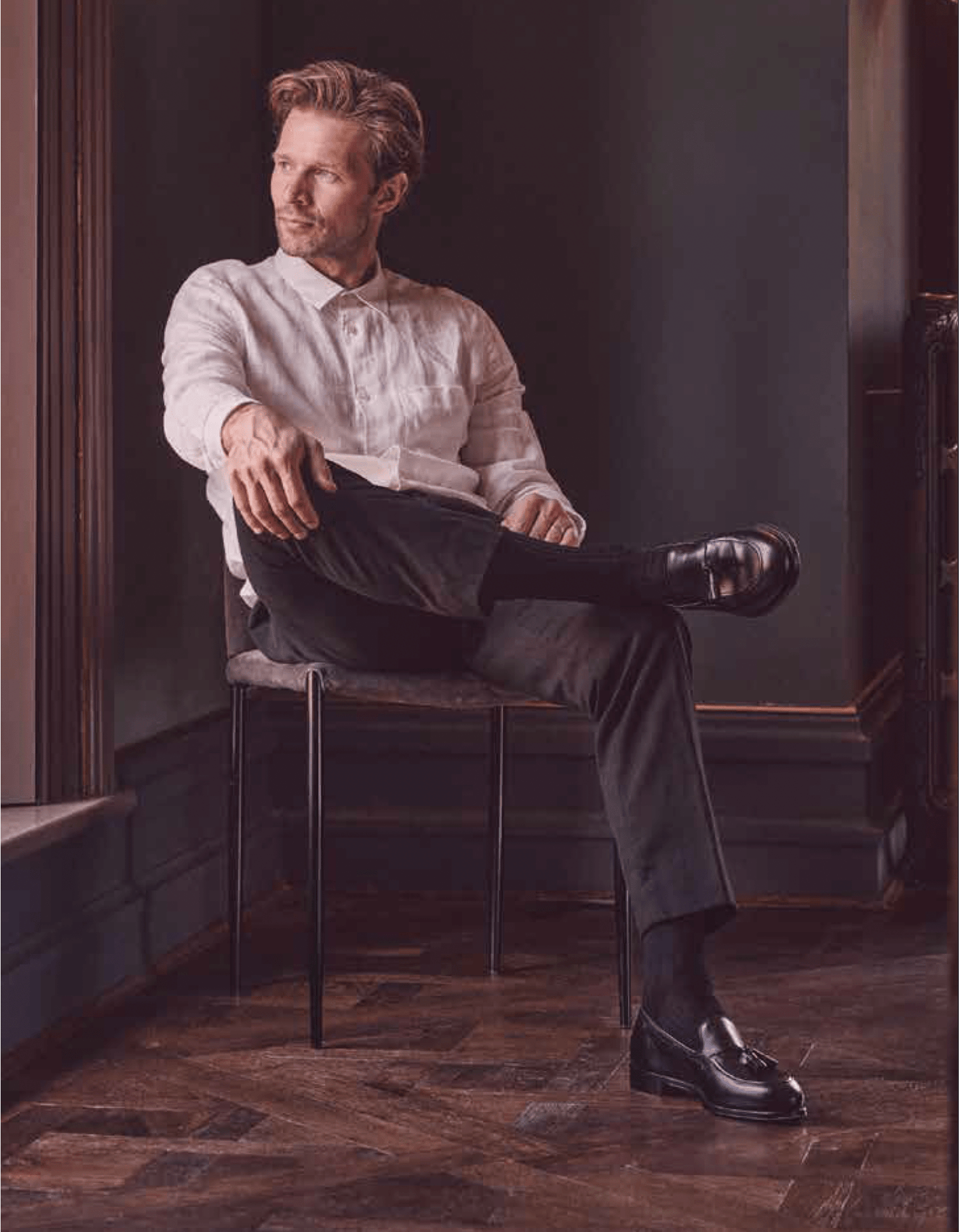 Man sitting on a chair in a room with dark walls and wooden floor.