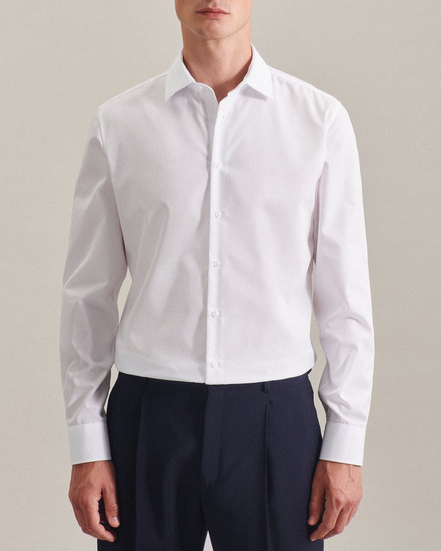 Person wearing a white dress shirt and navy pants against a plain background