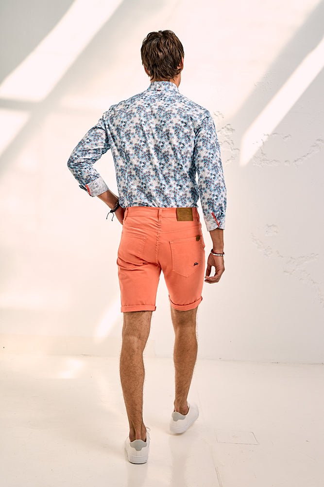 Man wearing a floral shirt and coral shorts on a white background